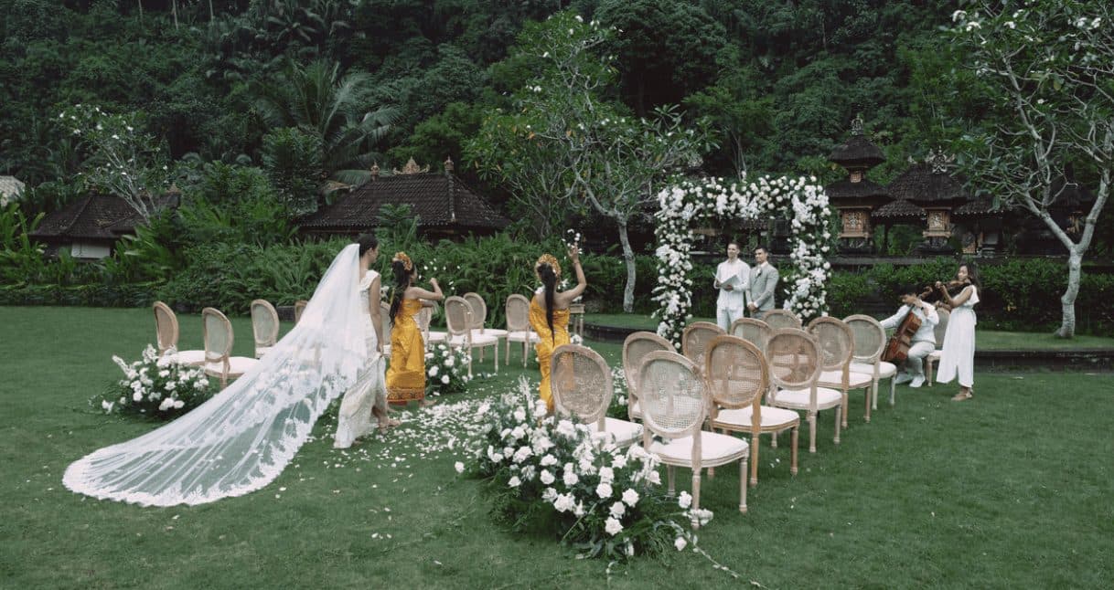 Mandapa, a Ritz-Carlton Reserve — a garden ceremony with the bride's veil trailing across the lawn · Ubud, Indonesia