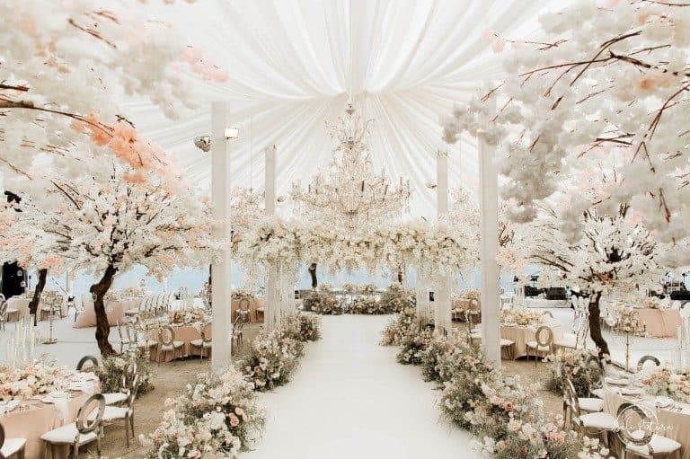 Six Senses Uluwatu — a reception beneath blossom trees and chandeliers in a draped marquee · Uluwatu, Indonesia