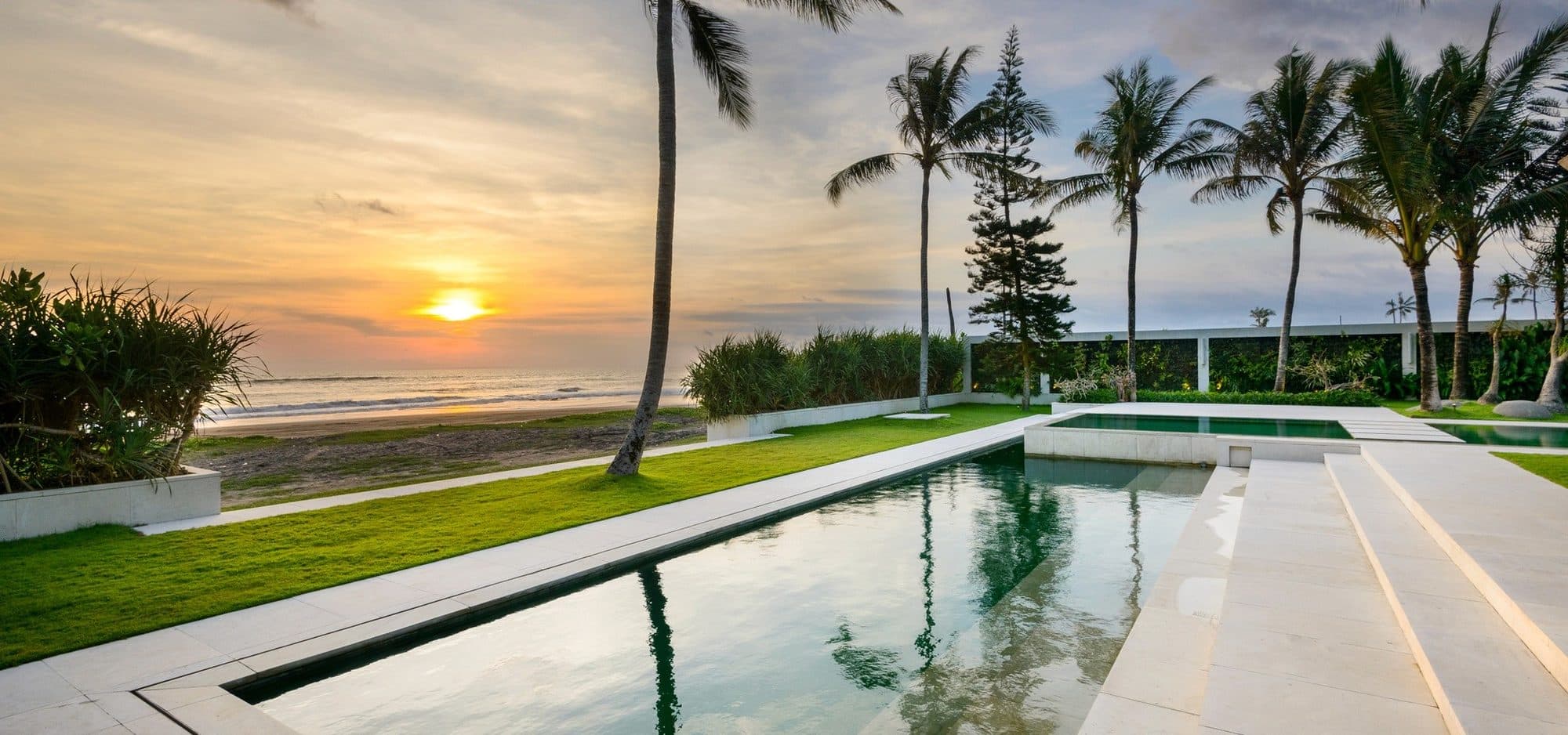 Villa Vedas — the pool at sunset, palms along the shore · Bali, Indonesia