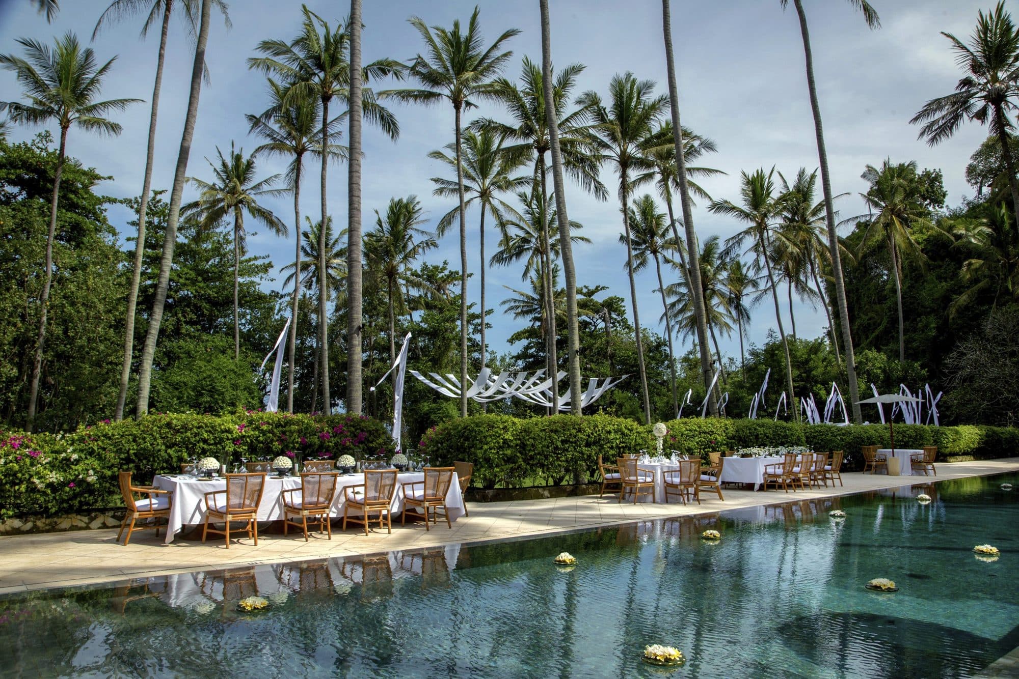 Amankila — a dinner set beside the pool beneath coconut palms · Manggis, Indonesia