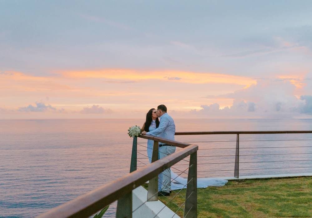 The Edge — a couple at the cliff railing at sunset · Uluwatu, Indonesia