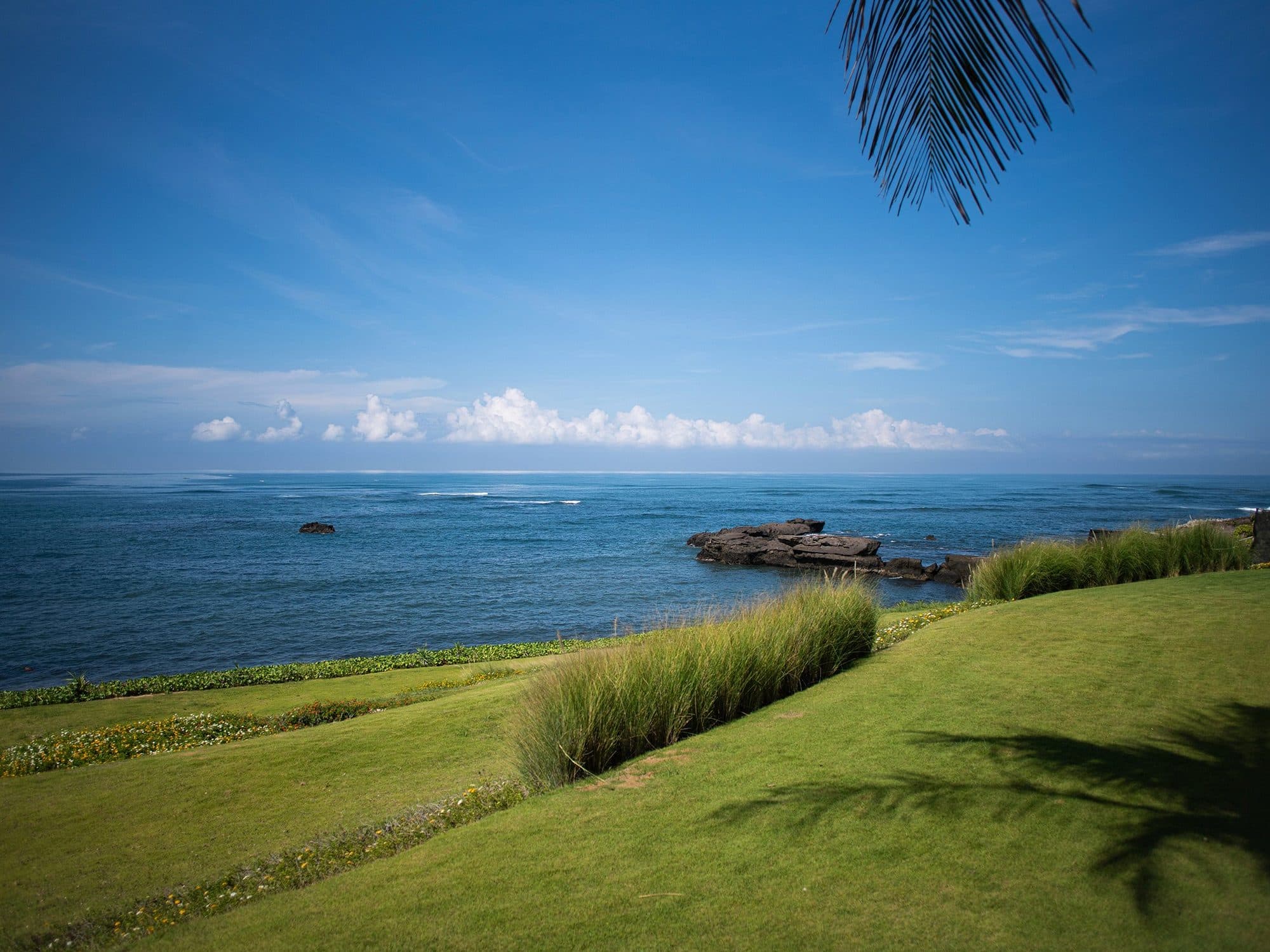 Tirtha Bayu Estate — the lawn running down to the rocky shore · Seseh, Indonesia