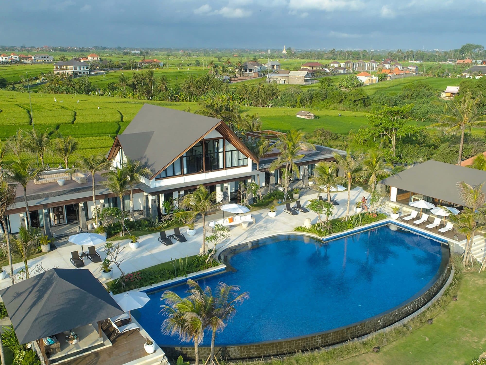 Tirtha Bayu Estate — aerial view of the curved pool, villas and rice fields · Seseh, Indonesia