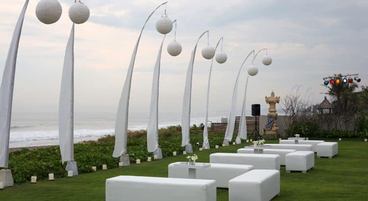Villa Phalosa — white lounge seating and tall penjor on the lawn above the beach · Seseh, Indonesia
