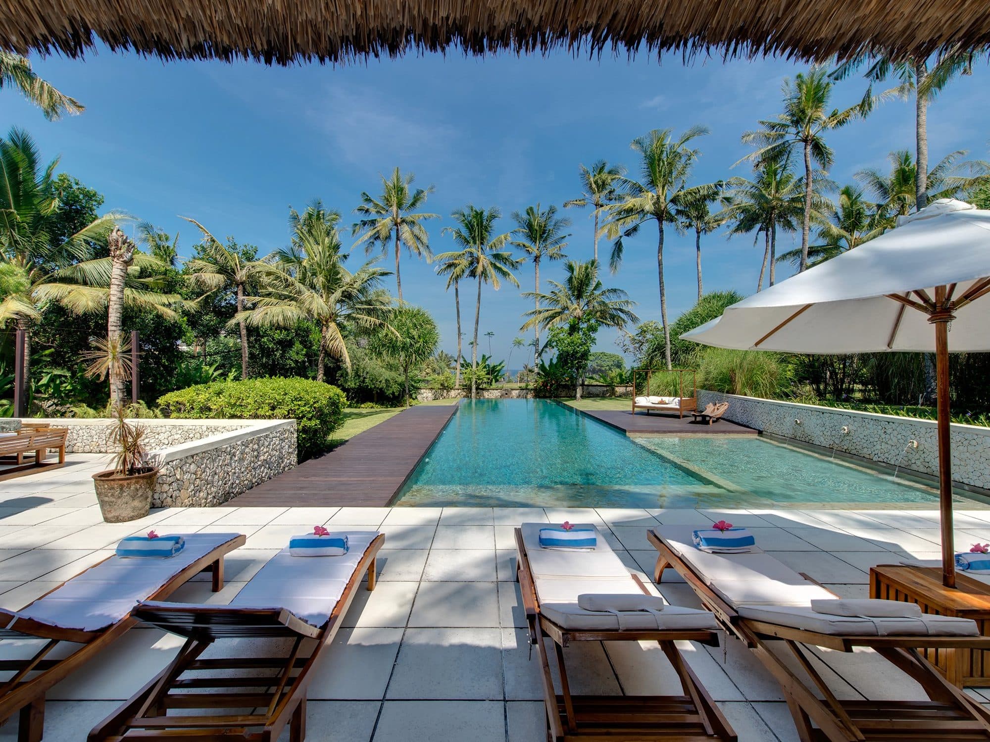 Villa Samadhana — loungers along the pool under a thatched roof · Ketewel, Indonesia