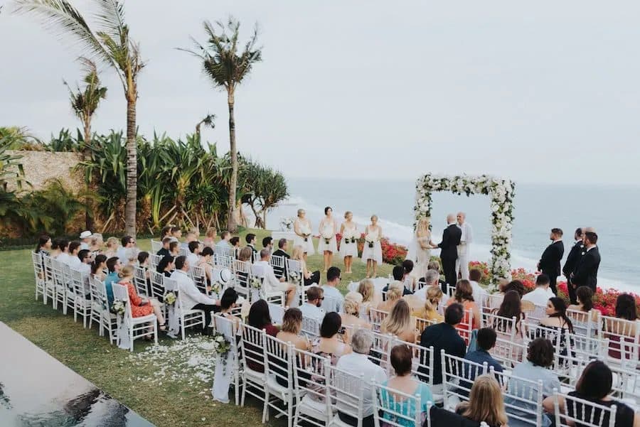 Villa Tamarama — a ceremony on the clifftop lawn beneath a floral arch · Bali, Indonesia